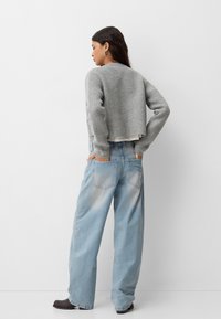Grey cropped sweater with round neckline and long sleeves, paired with loose light blue jeans featuring back pockets and faded detail.