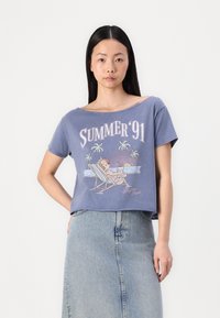 Skratka, plava majica s grafikom koja sadrži natpis "SUMMER '91" i crtani prizor plaže. Materijal izgleda mekano; opušteni kroj s kratkim rukavima.