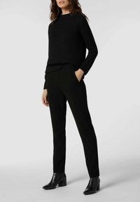 Maglione nero a coste con maniche lunghe abbinato a pantaloni neri sartoriali e stivaletti, creando un look monocromatico.