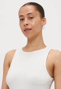 Top blanco sin mangas con un diseño ajustado, textura suave y escote redondeado. Presenta costuras sutiles y un aspecto limpio y minimalista.