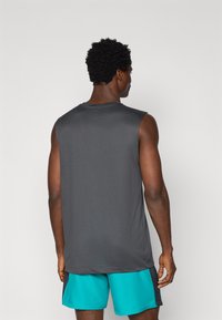 Graues ärmelloses Sportshirt mit rundem Ausschnitt, von hinten gezeigt, kombiniert mit türkisen Shorts mit schwarzen seitlichen Akzenten.