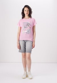 Pink short-sleeve t-shirt with a floral graphic print and the word "glow." Paired with gray denim shorts and white sneakers.