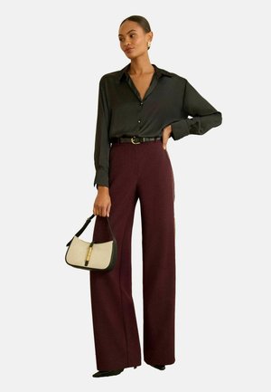 Dark button-up shirt paired with high-waisted burgundy wide-leg pants. The model holds a small handbag with a beige front and black trim.