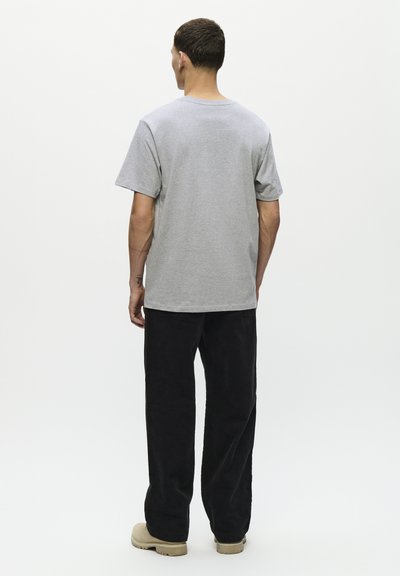 T-shirt en coton gris avec une coupe décontractée, des manches courtes et un col rond, associé à un pantalon en velours côtelé noir et des chaussures beiges.
