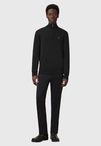 Sort zip-neck sweater i blødt stof med lange ærmer, parret med sorte tapered bukser og sorte ankelstøvler. Diskret logo detalje på brystet.