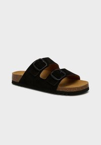 Svart mocka slide sandal med två justerbara remmar som har svarta spännen, en korkfotbädd och en texturerad gummisula.