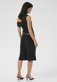 Zwarte aansluitende top met een off-shoulder ontwerp, gecombineerd met knielange zwarte shorts met een gladde textuur, voorzakken en een strakke riem.