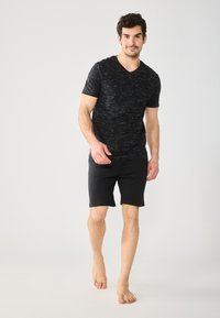 Black V-neck t-shirt with a textured, linear pattern, paired with black shorts. The outfit has a casual fit and is worn barefoot.