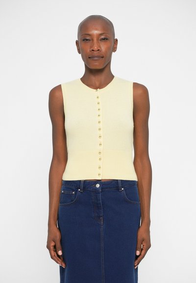 Haut sans manches jaune clair avec un col rond et des boutons dorés sur le devant, associé à une jupe en jean bleu foncé. Texture lisse.