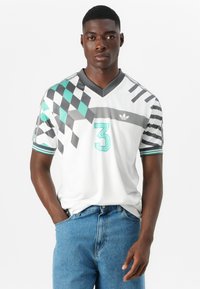 Fehér, rövid ujjú mez zöld és szürke geometrikus mintákkal, V-nyakkivágással és 3-as számmal az elején. Az adidas logója a mellkason található.