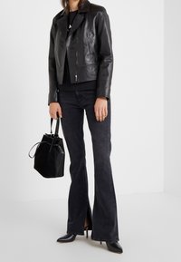 Svart läderbikerjacka med dragkedja, ihop med mörka utsvängda jeans och en svart bucket-väska. Inkluderar högklackade svarta skor.