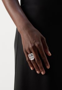 Clear rectangular ring on a hand, featuring a large faceted crystal with a smooth band, set against a black background.
