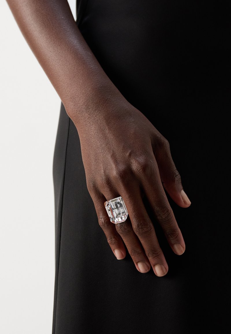 Clear rectangular ring on a hand, featuring a large faceted crystal with a smooth band, set against a black background.