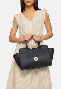Black leather handbag with textured surface, structured shape, short handles, and a gold hardware accent on the front.
