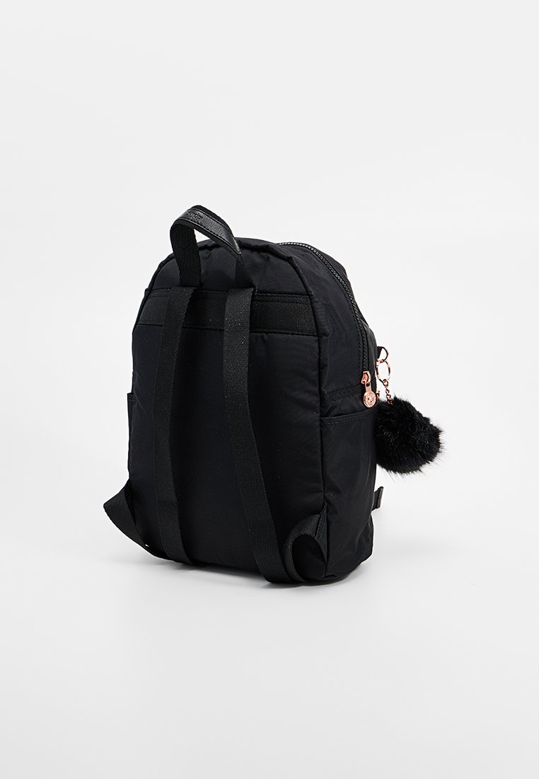 Zaino in nylon nero con due spallacci, chiusura con zip, tasca frontale e un accessorio pom-pom nero attaccato. Forma compatta e rettangolare.