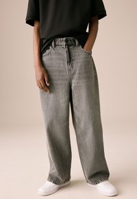 Wijde grijze spijkerbroek met een hoge taille, ontwerp met vijf zakken, zichtbare stiksels en subtiele textuur, gecombineerd met witte sneakers.