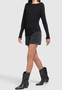 Haut noir à manches longues associé à un short noir. Chaussures composées de bottes de cow-boy noires ajustées, à bout pointu et talon bas.