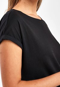 T-shirt noir à manches courtes avec revers roulés, en tissu de coton doux. Encolure ronde avec une coupe décontractée et une texture lisse.