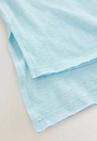 Világoskék szövet dupla rétegű szegéllyel és oldalsó hasíték részlettel, textúra és varrás közelről.