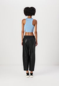 Lichtblauwe mouwloze crop top gecombineerd met zwarte, loszittende, glanzende broek en zwart-witte sneakers. Eenvoudig ontwerp met elastische tailleband.