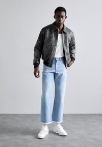 Sort, tekstureret bomberjakke med krave, parret med lyseblå, vide jeans. Hvide sneakers fuldender outfittet.