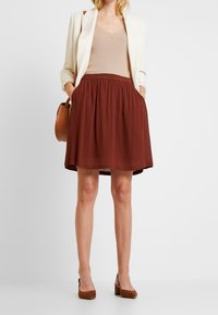 En vinröd kjol i lätt tyg med resårmidja, kombinerad med en beige topp och en krämfärgad blazer med texturerade ytor.