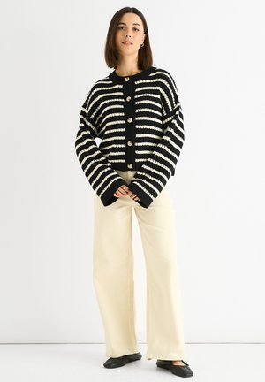 Black and white striped cardigan with a round neckline, featuring large buttons and wide sleeves. Paired with cream wide-leg pants.