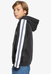 Sudadera negra con mangas a rayas blancas y azules, bolsillo frontal tipo canguro y capucha con cordones. Material suave y texturizado.