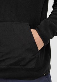 Schwarzer Fleece-Pullover mit strukturiertem Finish, ausgestattet mit einer Kängurutasche, gerippten Bündchen und einem kleinen Logo-Tag am Saum.