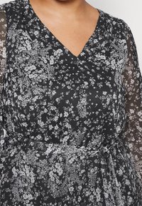 Vestido negro con estampado floral y escote en V, que presenta un diseño de mangas largas transparentes, detalles de botones y un lazo en la cintura ceñido. Flores en colores blanco y gris.