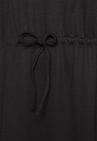 Tecido preto com uma textura suave, apresentando uma cintura franzida e um detalhe de cordão amarrado. Detalhe de design simples e funcional.