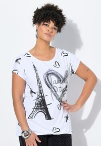 Camiseta blanca con gráficos en negro y plateado, que incluyen la Torre Eiffel y corazones, con mangas cortas y un corte relajado.