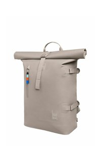 Mochila roll-top beige hecha de material resistente al agua. Cuenta con correas ajustables, un bolsillo con cremallera en la parte frontal y un logotipo en el costado.