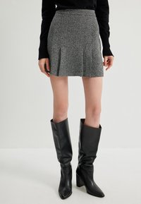 Falda mini texturizada gris con pliegues, combinada con botas de cuero negras hasta la rodilla con punta cuadrada y tacón cuadrado.