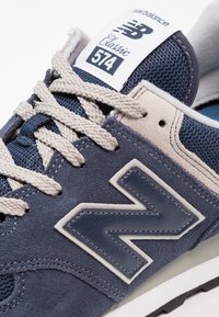 Új Balance 574 sneaker sötétkék színben, világosszürke velúrral és hálós anyaggal. Klasszikus fehér logóval, texturált cipőfűzőkkel és gumitalppal rendelkezik.