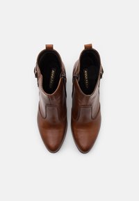 Hnědé kožené kotníkové boty s špičatou špičkou, bočním zipem a jemnými vyšívacími detaily. Interiér je podšitý měkkým černým materiálem.