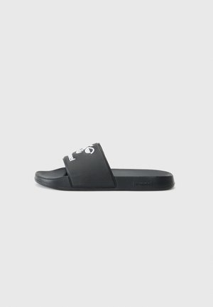 Zwarte rubberen slide-sandalen met een brede band met een wit logo, vlakke zool en een gladde structuur. Minimalistisch ontwerp.