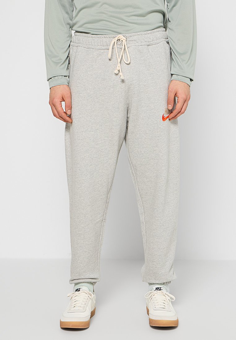Pantalons de survêtement gris en coton avec une taille élastique et un cordon de serrage, présentant un petit logo Nike orange sur la cuisse gauche.