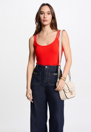 Red tank top with lace detailing on straps, paired with high-waisted dark denim wide-leg pants. Beige crossbody bag with gold hardware.