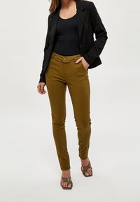 Olivgrön figursydda byxor med en slät textur, knäppning framtill och sidofickor, tillsammans med en svart topp och blazer.