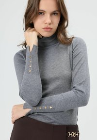 Grijze coltrui gemaakt van zachte stof, met gouden knoopdetails op de mouwen en een getailleerd model.