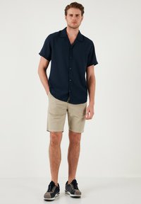 Korte mouwen marineblauw overhemd met knopen, gecombineerd met beige shorts en zwarte sneakers, met een soepele stof en een relaxte pasvorm.