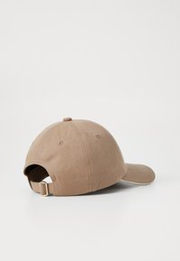Brown cotton cap with curved visor, adjustable strap at back, and soft texture. Features a rounded top and stitching detail.
