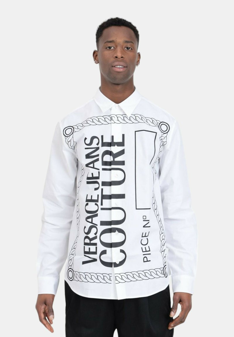 Witte overhemddress met gedurfde zwarte tekst en kettinggrafiek ontwerp. Lange mouwen met knopen bij de manchetten. Minimalistische, hedendaagse stijl.