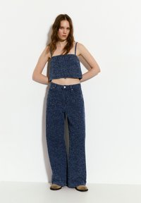 Modrý puntíkovaný cropped top s tenkými ramínky a vysokým pasem široké kalhoty ze stejných materiálů. Měkká textilie a volný střih po celém kroji.