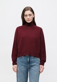 Bordowy golf o luźnym kroju z prążkowanymi mankietami i dołem, zestawiony ze światłoniebieskimi, postrzępionymi dżinsami. Miękka faktura, design sięgający do połowy tułowia.