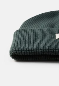 Gorro de malha canelada em turquesa, dobrado na bainha, apresentando uma pequena etiqueta de tecido. Textura suave com um ajuste justo, adequado para o tempo frio.