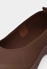 Κοντινό πλάνο ενός καφέ παπουτσιού χωρίς κορδόνια με υφασμάτινο επάνω μέρος με υφή και μικρή θηλιά πίσω στη φτέρνα.