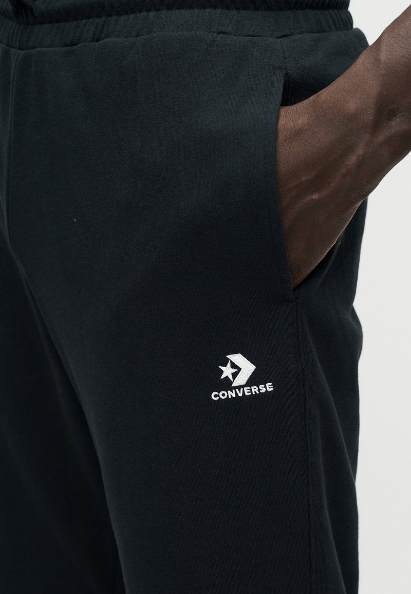 Sorte bomuldsjoggebukser med sidelommer og et hvidt broderet Converse-logo, med en glat tekstur og elastisk talje.