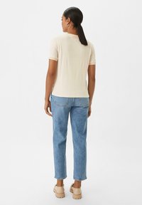 T-shirt beige chiaro a maniche corte con scollatura rotonda, abbinato a jeans dritti blu chiaro e scarpe chunky beige.